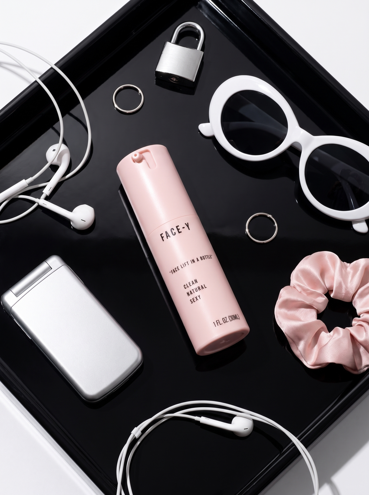 Face-y bottle with sunglasses and earbuds on a black tray